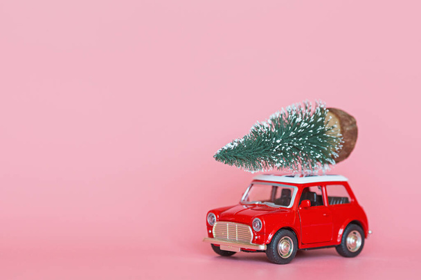 Changxing, China - October 15, 2019: Red toy car with a christmas tree on the roof on pink paper background. Winter delivery, xmas, happy new year 2020 celebration concept. greeting card, mockup - Photo, Image