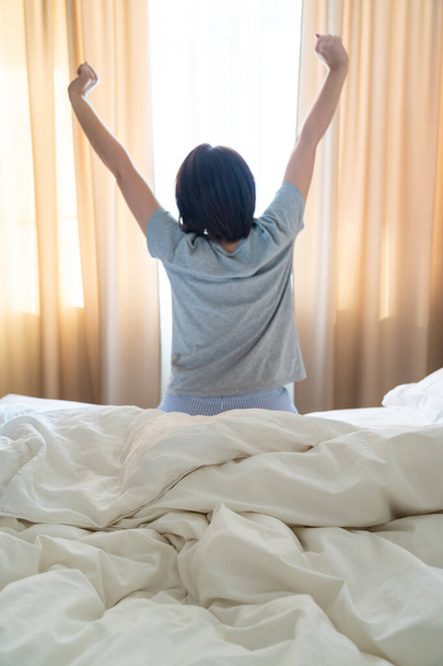 Жінка розтягується в ліжку після пробудження, вид ззаду
 - Фото, зображення