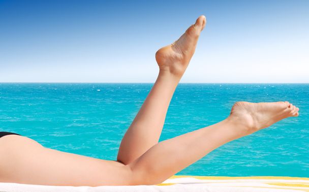 sexy vrouwelijke benen tegen turquoise zee - Foto, afbeelding