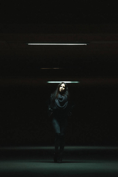 Портрет девушки с длинными черными волосами в темной одежде в ночном городе. Девушка на тёмной парковке. Портрет в темном ключе в городе
 - Фото, изображение