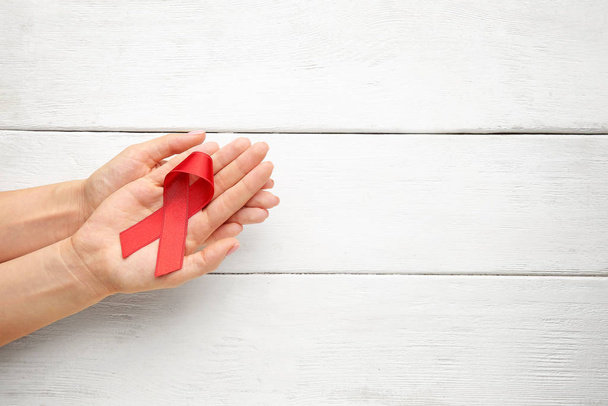 Female hands with red ribbon on white wooden background. AID awareness concept - Photo, Image