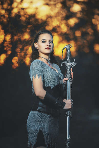 Tyttö ritari ketjupostissa miekka cosplay goottilainen tyyli. Soturi Amazon kuva Halloween. Nainen, jolla on lohikäärmeen muotoinen miekka ja kahva.
. - Valokuva, kuva