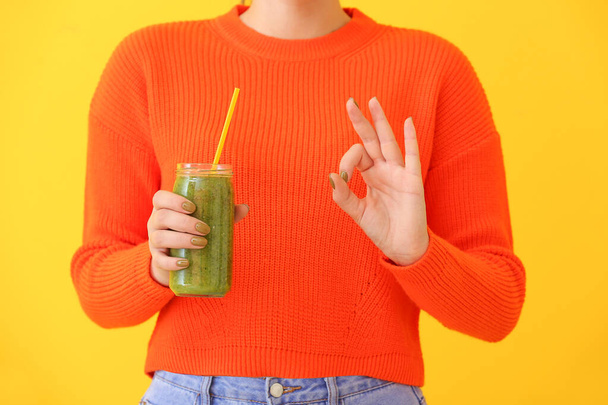Woman with jar of healthy smoothie showing OK on color background - Foto, Bild