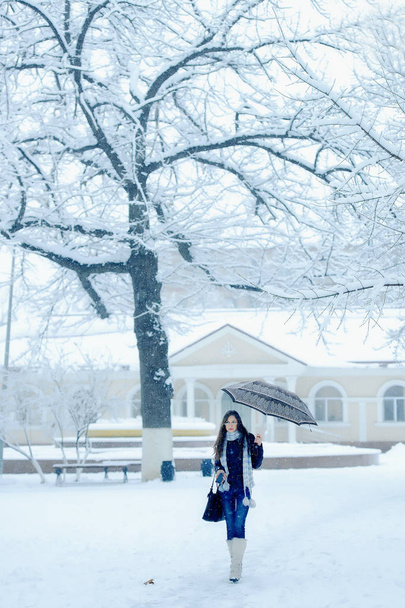 Girls with umbrella under snowfall in winter outdoor in the city. Romantic girl in glasses for vision on the street in winter under the snow. Beautiful young brunette woman in winter landscape - Photo, Image