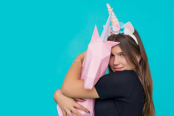 Kawaii teenage girl. Cute young woman with unicorn horn holding and hugging handmade paper pink unicorn over blue background. - 写真・画像