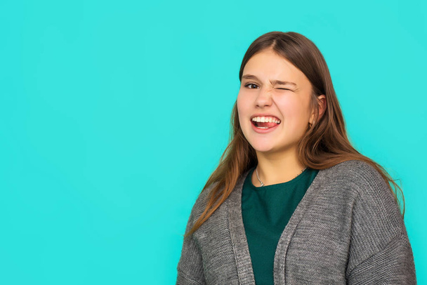 Zdjęcie z głowy Portret szczęśliwej nastoletniej rudej dziewczyny z uśmiechem patrzącej w kamerę. Niebieskie tło. portret pięknej młodej kobiety mrugającej - Zdjęcie, obraz