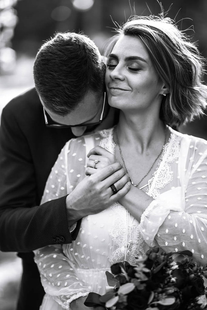 Beautiful black and white photo of bride and groom. Happy couple posing and smiling in wedding dress and suit with bridal bouquet in the park. People enjoy each other. Together. Wedding concept. - Valokuva, kuva