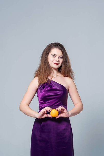 A girl in a purple dress on a white background with tangerines in her hands. Small oranges in the hands of girls. Tangerines in the hands of a woman on a white background - Foto, Imagem