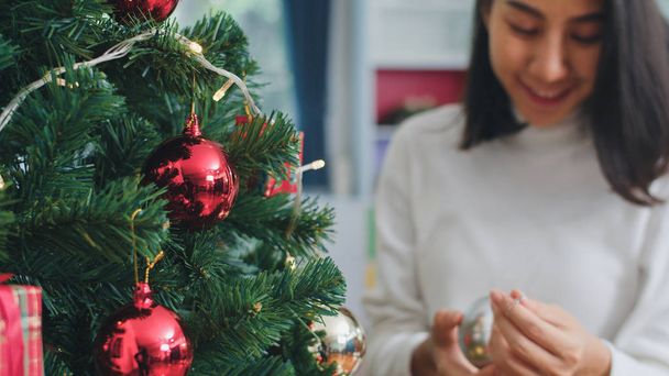 Mulheres asiáticas decoram a árvore de Natal no festival de Natal. Adolescente feminino feliz sorrindo comemorar xmas férias de inverno na sala de estar em casa. Fechar tiro
. - Foto, Imagem