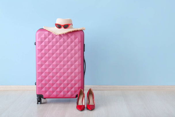 Packed suitcase, female hat and shoes near color wall. Travel concept - Photo, Image