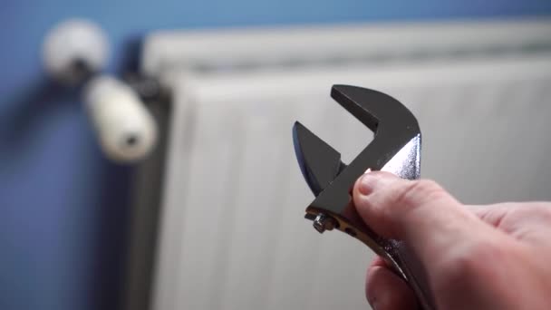 Regulowany klucz w dłoni męskiego mechanika na tle białego grzejnika na niebieskiej ścianie. Naprawa i montaż instalacji grzewczej w budynku mieszkalnym - Materiał filmowy, wideo