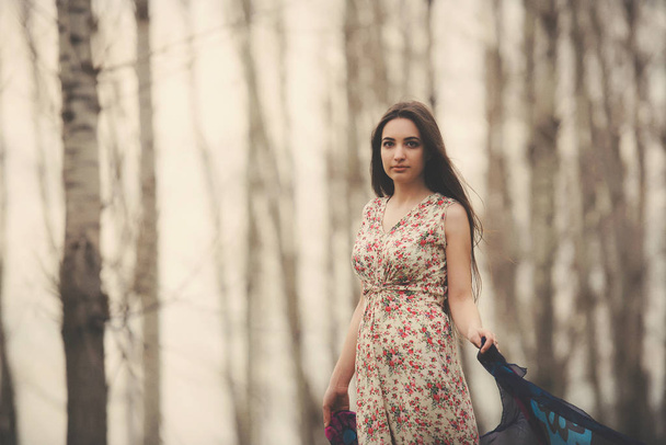 Baharın başında bir bahçede güzel bir genç kadının portresi. Huş ağacından bir korulukta açık renk elbiseli esmer kız. Esmer kız ormanda yürüyor - Fotoğraf, Görsel