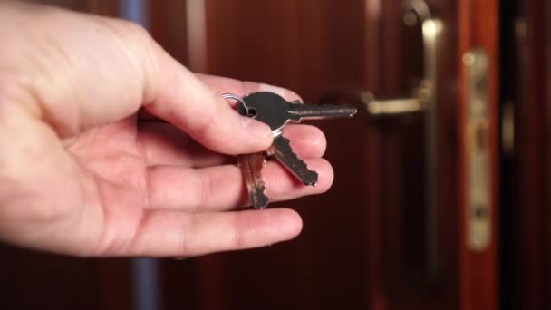 Shiny new keys to the apartment in the mans hand and ajar brown lacquered lacquered door with a handle and a lock of bronze color. Security Hacking Concept - Кадры, видео