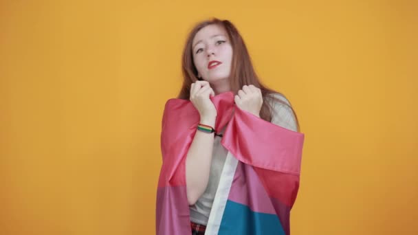 Young woman keeping thumbs on cheeks, covered bisexual flag. - Materiał filmowy, wideo