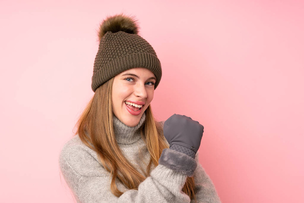 Young teenager girl with winter hat over isolated pink background celebrating a victory - Photo, image