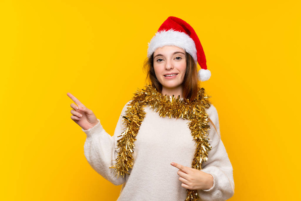 Girl with christmas hat over isolated yellow background pointing finger to the side - Photo, Image