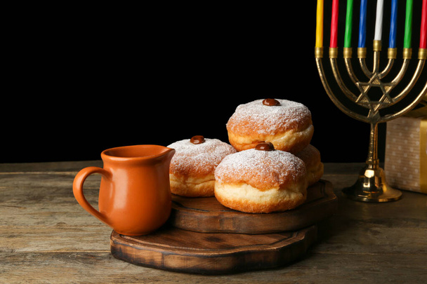 Menorah and donuts for Hanukkah on table against dark background - Foto, afbeelding