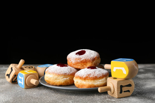 Donuts for Hanukkah and dreidels on table against dark background - Photo, Image