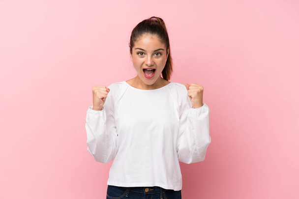 Young brunette girl over isolated pink background celebrating a victory in winner position - Φωτογραφία, εικόνα