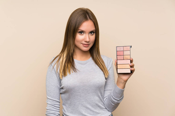 Teenager dívka s make-up paleta přes izolované pozadí s úsměvem hodně - Fotografie, Obrázek