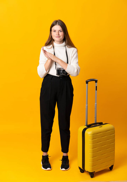 Volledig lichaam van reiziger tiener meisje met koffer over geïsoleerde gele achtergrond applaudisseren - Foto, afbeelding