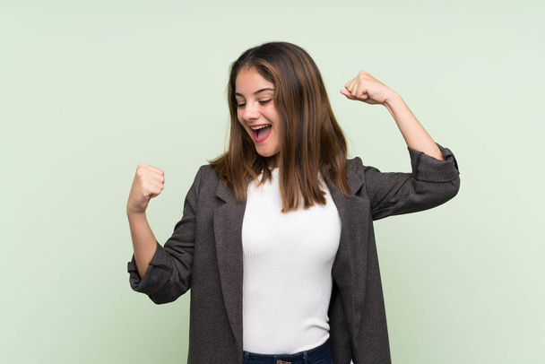 Young brunette girl with blazer over isolated green background celebrating a victory - Photo, Image