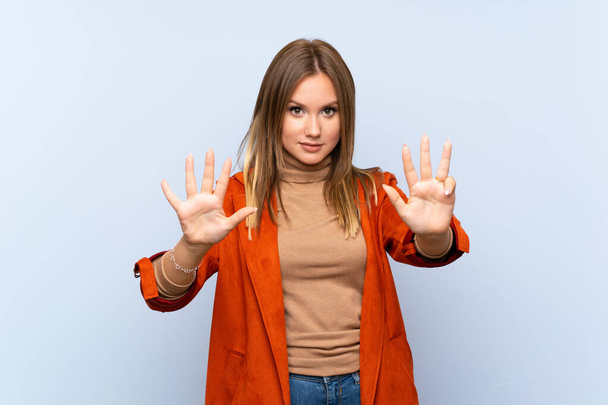 Teenager girl with coat over isolated blue background counting nine with fingers - Фото, зображення
