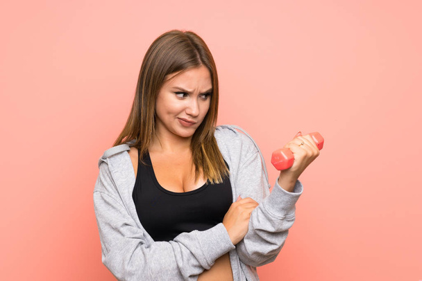 Teenager sport girl making weightlifting over isolated pink background with sad expression - 写真・画像