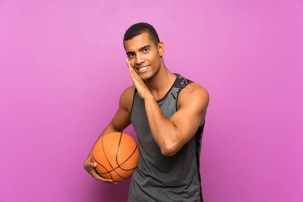 Jonge sportman met basketbal over geïsoleerde paarse muur fluisterend iets - Foto, afbeelding