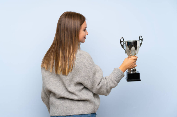 Ragazza adolescente con maglione su sfondo blu isolato in possesso di un trofeo
 - Foto, immagini