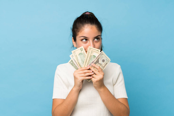 Mladá brunetka dívka přes izolované modré pozadí přičemž spoustu peněz - Fotografie, Obrázek