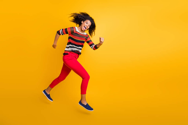 Full length profile side photo of crazy funky girl jump run hurry after autumn fall black friday bargains feel excited scream wear red pants trousers isolated over yellow color background - Fotografie, Obrázek