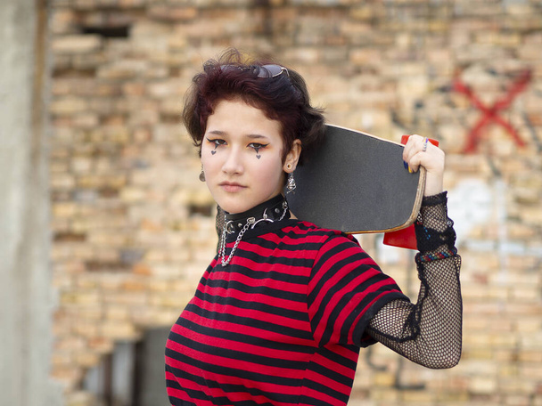 Chica patinadora gótica posando en la calle con monopatín en los hombros efecto bokeh
 - Foto, imagen