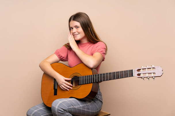 Украинская девушка-подросток с гитарой на изолированном фоне шепчет что-то
 - Фото, изображение