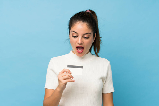 Giovane ragazza bruna su sfondo blu isolato in possesso di una carta di credito
 - Foto, immagini