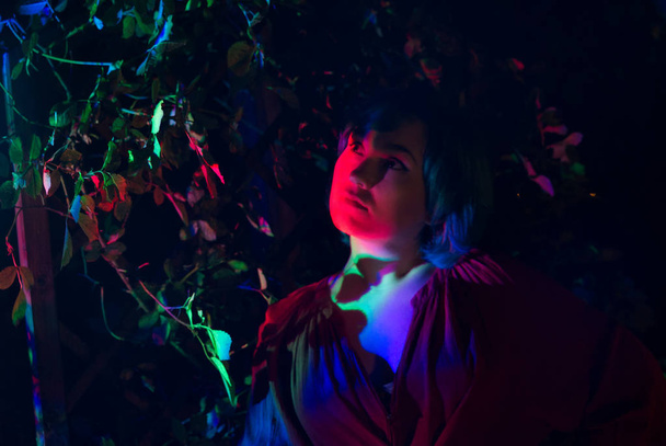 Young woman in the garden illuminated by multi-colored light. - Фото, изображение