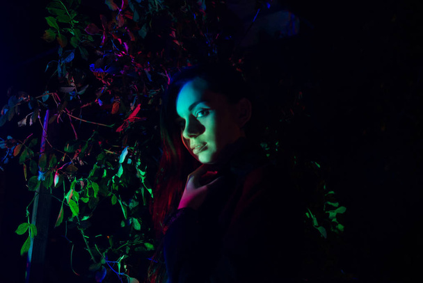 Kobieta w lesie oświetlona wielokolorowym światłem - noir. - Zdjęcie, obraz