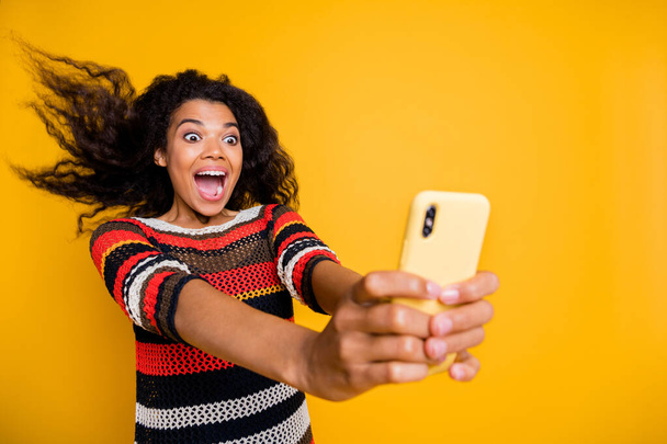 Portrait of positive cheerful afro american girl blogger ride roller coaster have her hair fly make selfie blogging video calling scream wow omg wear striped shirt isolated yellow color background - Foto, immagini