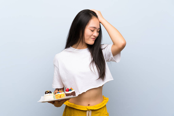 Teenager asian girl holding lots of different mini cakes has realized something and intending the solution - Fotó, kép