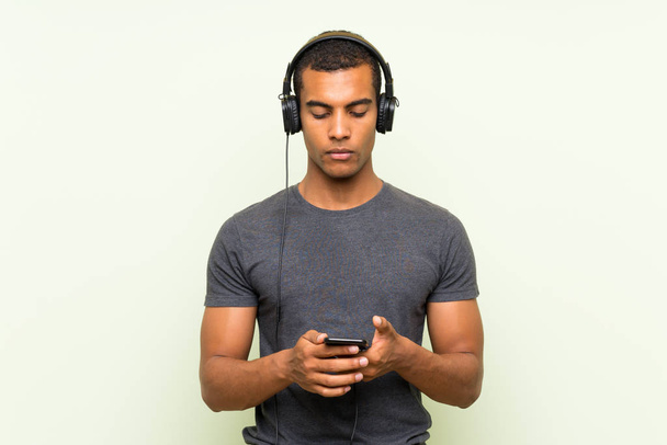 Молодой красивый мужчина слушает музыку с мобильного над изолированной зеленой стеной
 - Фото, изображение