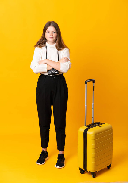 Полное тело путешествующей девочки-подростка с чемоданом на изолированном желтом фоне, держащего руки скрещенными
 - Фото, изображение