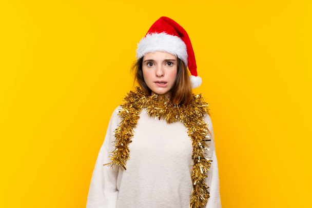 Girl with christmas hat over isolated yellow background having doubts and with confuse face expression - Fotoğraf, Görsel