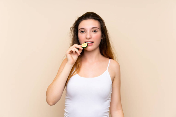 Young brunette girl holding slices of cucumber over isolated background - Фото, зображення