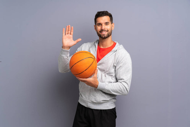 schöner junger Basketballspieler, der mit glücklicher Miene mit der Hand salutiert - Foto, Bild