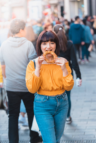 Симпатичная девушка ест турецкий уличный фаст-фуд симит
 - Фото, изображение
