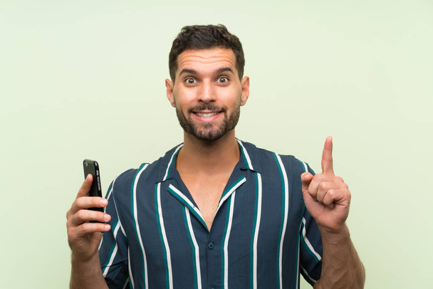 Young handsome man with a mobile pointing up a great idea - Фото, изображение