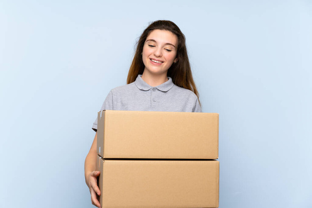 Fiatal barna lány több mint elszigetelt kék háttér kezében egy doboz mozgatni egy másik helyre - Fotó, kép