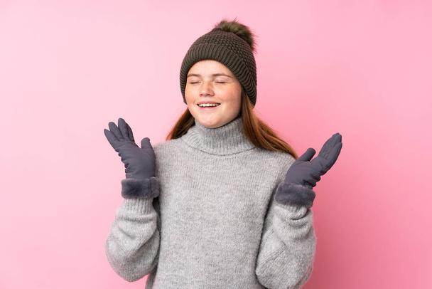 Українська дівчинка-підліток з зимовим капелюхом над ізольованим рожевим фоном сміється - Фото, зображення