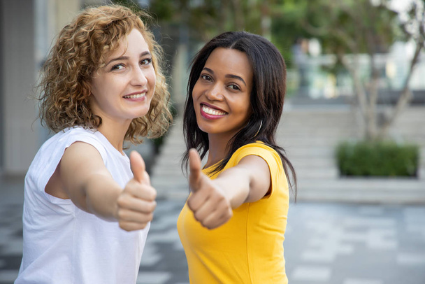 Portret dwóch szczęśliwych, wielonarodowych kobiet oddających kciuk w górę; biała kobieta z afrykańską kobietą wykazująca się dobrą, tak, akceptującą, pozytywną, aprobującą gest kciuka w górę - Zdjęcie, obraz