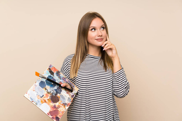Teenager Mädchen mit einer Palette über isolierten Hintergrund denken eine Idee - Foto, Bild